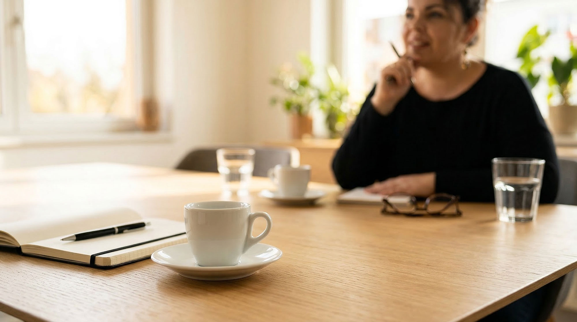 Espressotasse und Notizbuch auf einem Besprechungstisch, Yvonne Bläsing im Hintergrund